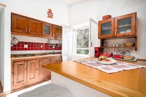 Une cuisine avec des meubles en bois, un crédence en carreaux rouges, une grande fenêtre et un îlot central agrémenté d’un set de table.