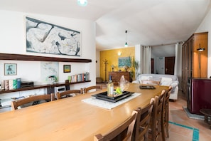 A dining area with a wooden table, chairs, a bookshelf, and a painting on the wall.