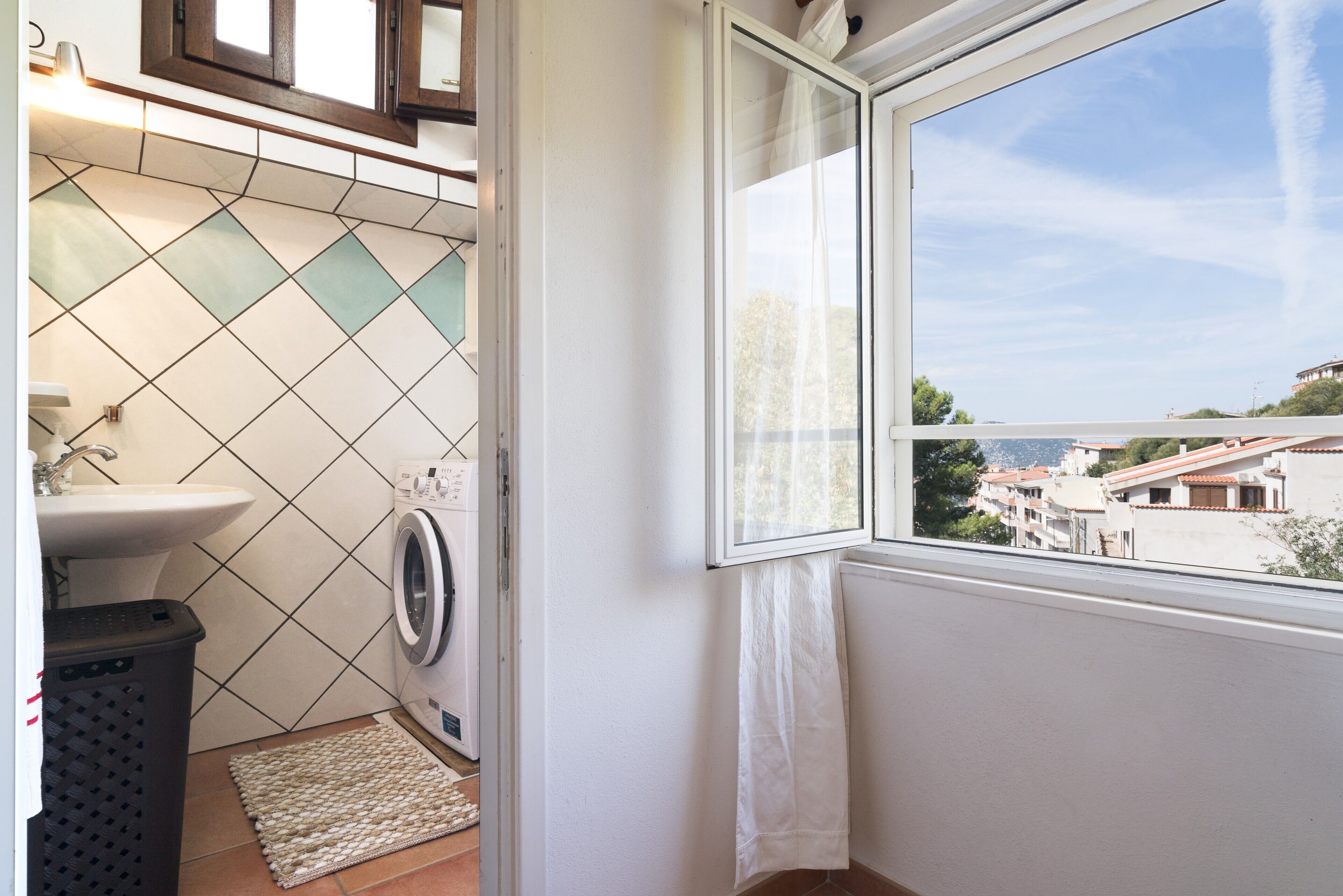 A laundry area with a washing machine, a sink, and a window with a view of buildings.