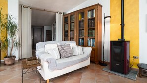 A living room with a sofa, a bookshelf, a fireplace, and a potted plant. - Holiday Apartment "Casa Su Craminu" with Mountain View, Balcony & Wi-Fi (Dorgali)