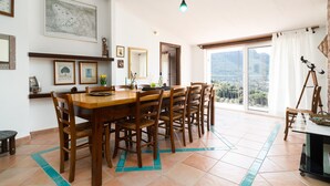 A dining area with a wooden table and chairs, a large window with a mountain view, and a painting on the wall. - Holiday Apartment "Casa Su Craminu" with Mountain View, Balcony & Wi-Fi (Dorgali)