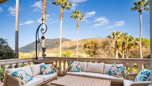 A covered outdoor seating area with a sofa and table, surrounded by tall palm trees and a mountainous backdrop. - Villa "Son Simo D'Alt" with Mountain View, Private Pool & Wi-Fi (Crestatx)