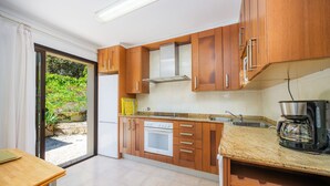 A kitchen with wooden cabinets, a white oven, a coffee maker, and a sliding glass door leading to a garden. - Holiday Home 'Can Bennassar' with Private Terrace, Balcony and Wi-Fi (Cala Sant Vicenç)