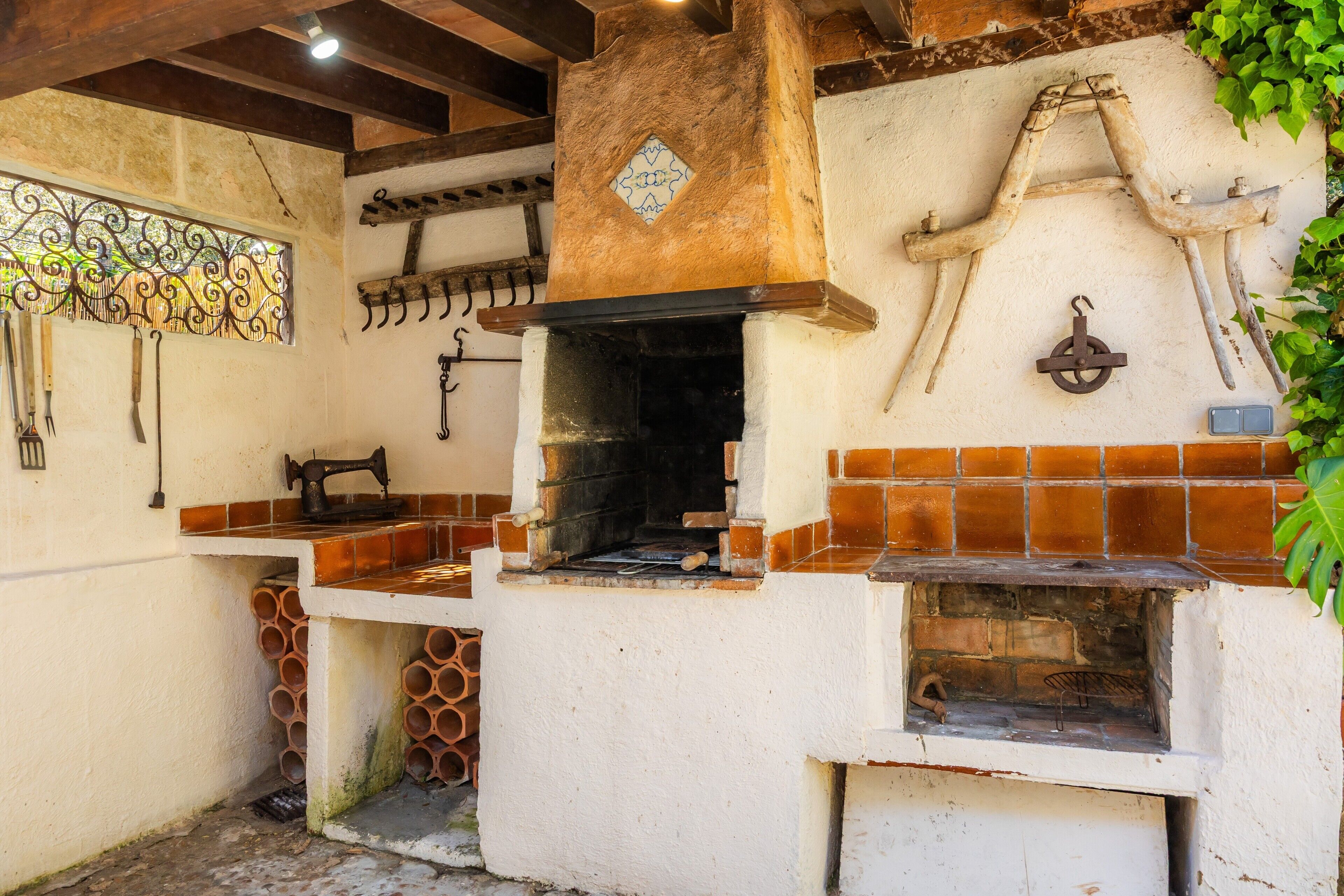 A rustic outdoor kitchen with a brick oven, hanging tools, and a decorative tile wall.