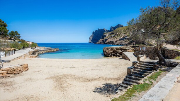A beach with clear blue water, a stone staircase, and a rocky cliff. - Holiday Home 'Can Bennassar' with Private Terrace, Balcony and Wi-Fi (Cala Sant Vicenç)