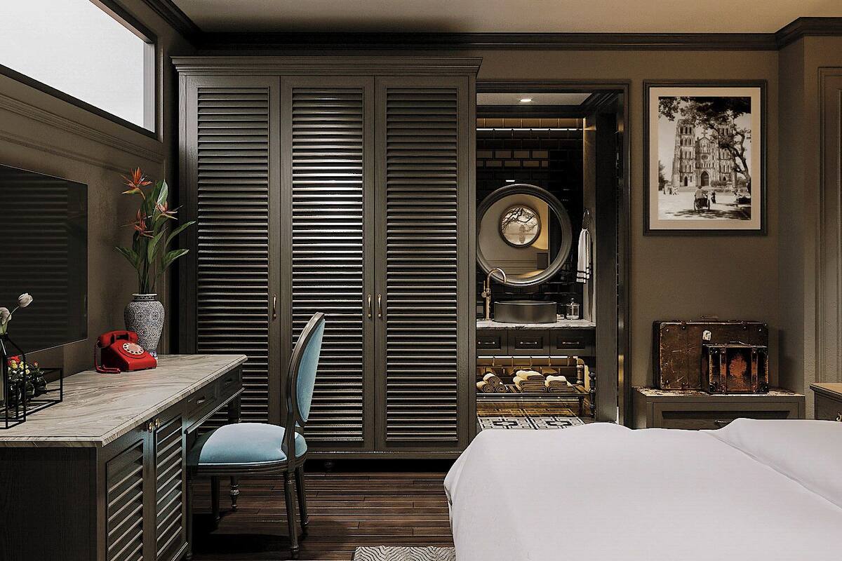 A bedroom with a bed, a desk with a chair, a vanity with a mirror, and a wardrobe.