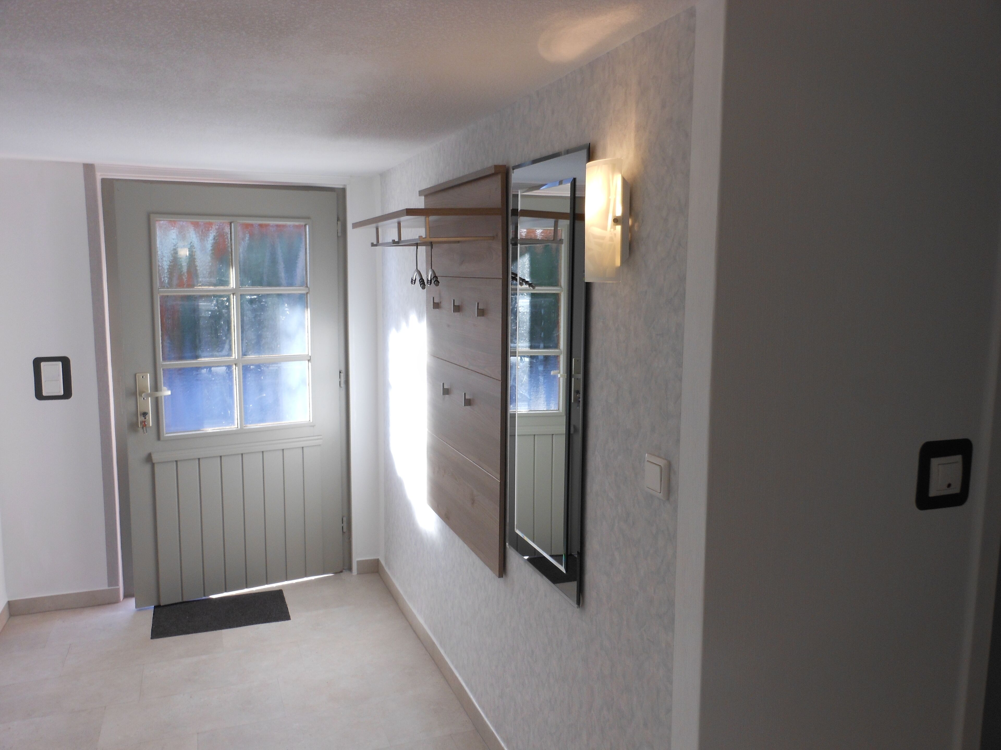 A hallway with a door, a coat rack, and a wall-mounted mirror.