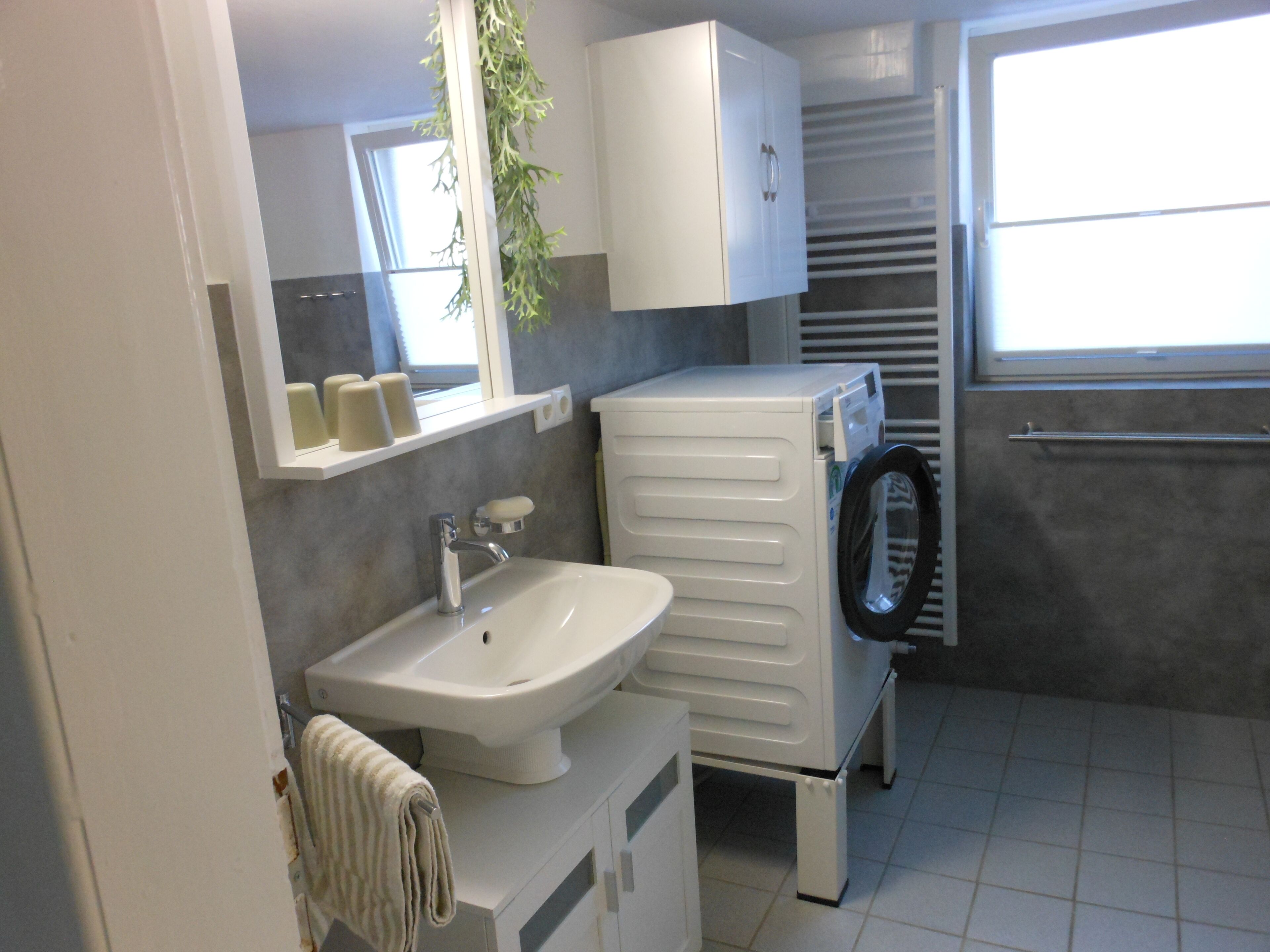 A compact bathroom with a white sink, a mirror, a towel rack, and a small window.