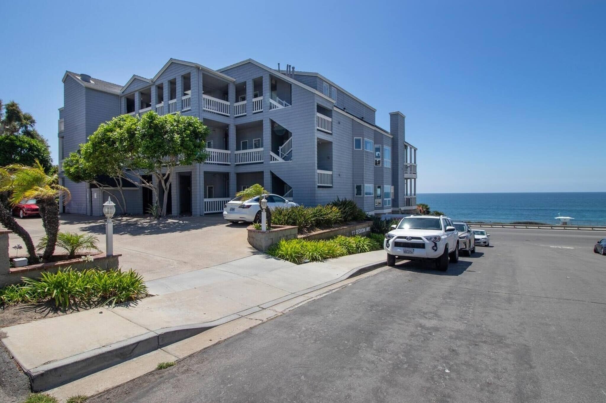 A multi-story building with balconies, a parking area, and a view of the ocean.
