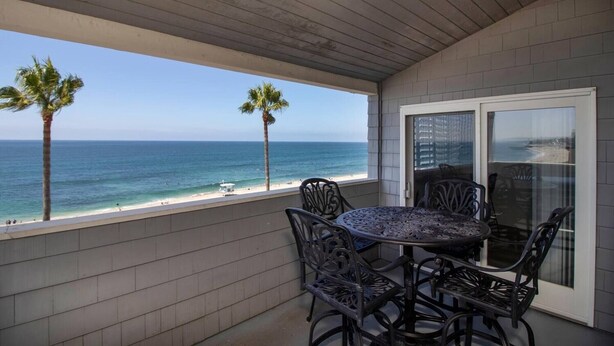 Een balkon met uitzicht op de oceaan, een ronde tafel met stoelen en twee palmbomen.