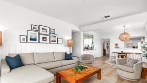 Een moderne woonkamer met een hoekbank, een houten salontafel en een eethoek met een tafel en stoelen.