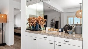 Een moderne keuken met witte kasten, een grote spiegel en een decoratieve vaas met gedroogde bladeren.
