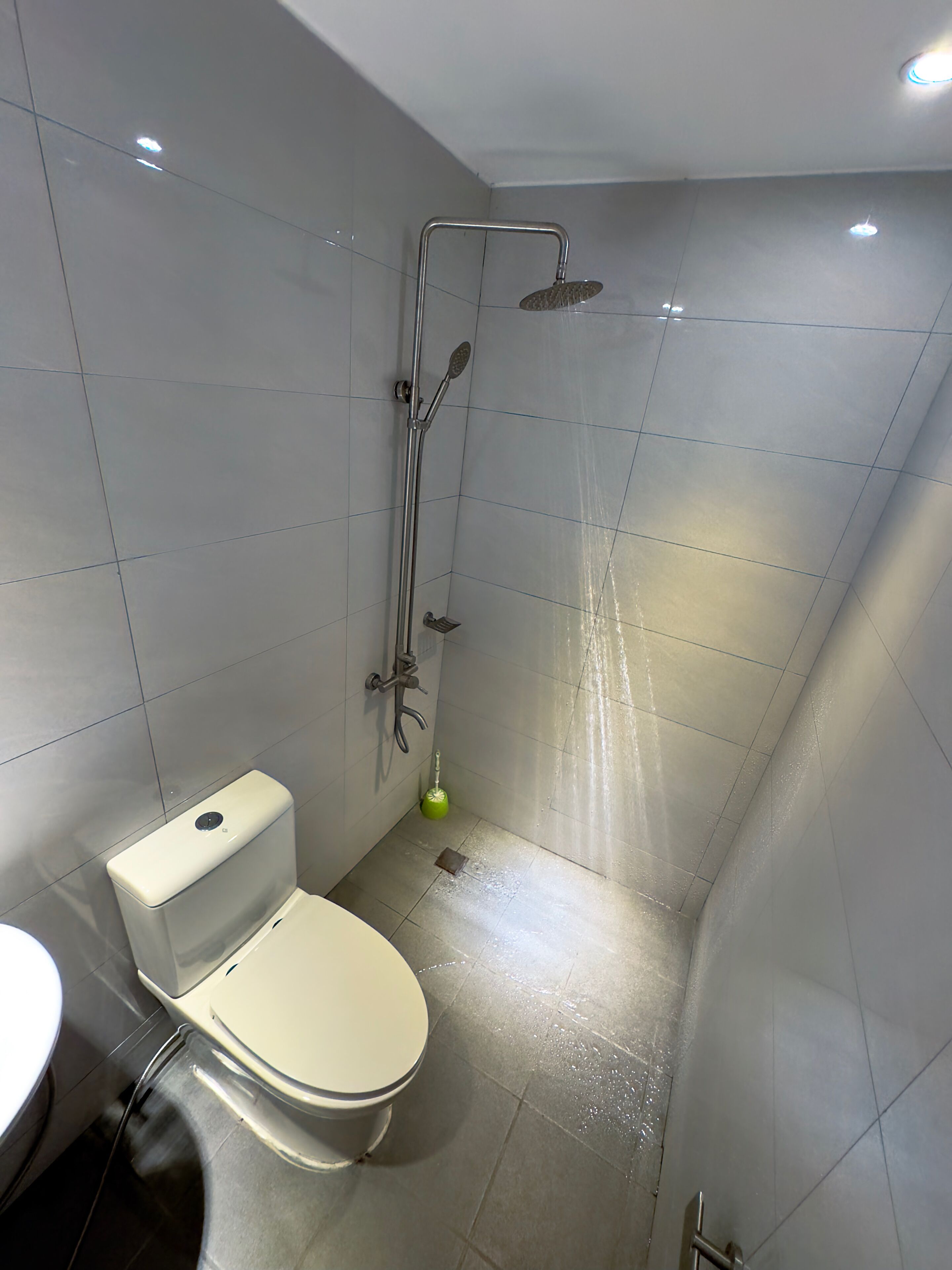 Un baño moderno con inodoro, ducha y un cepillo de limpieza verde en el suelo.