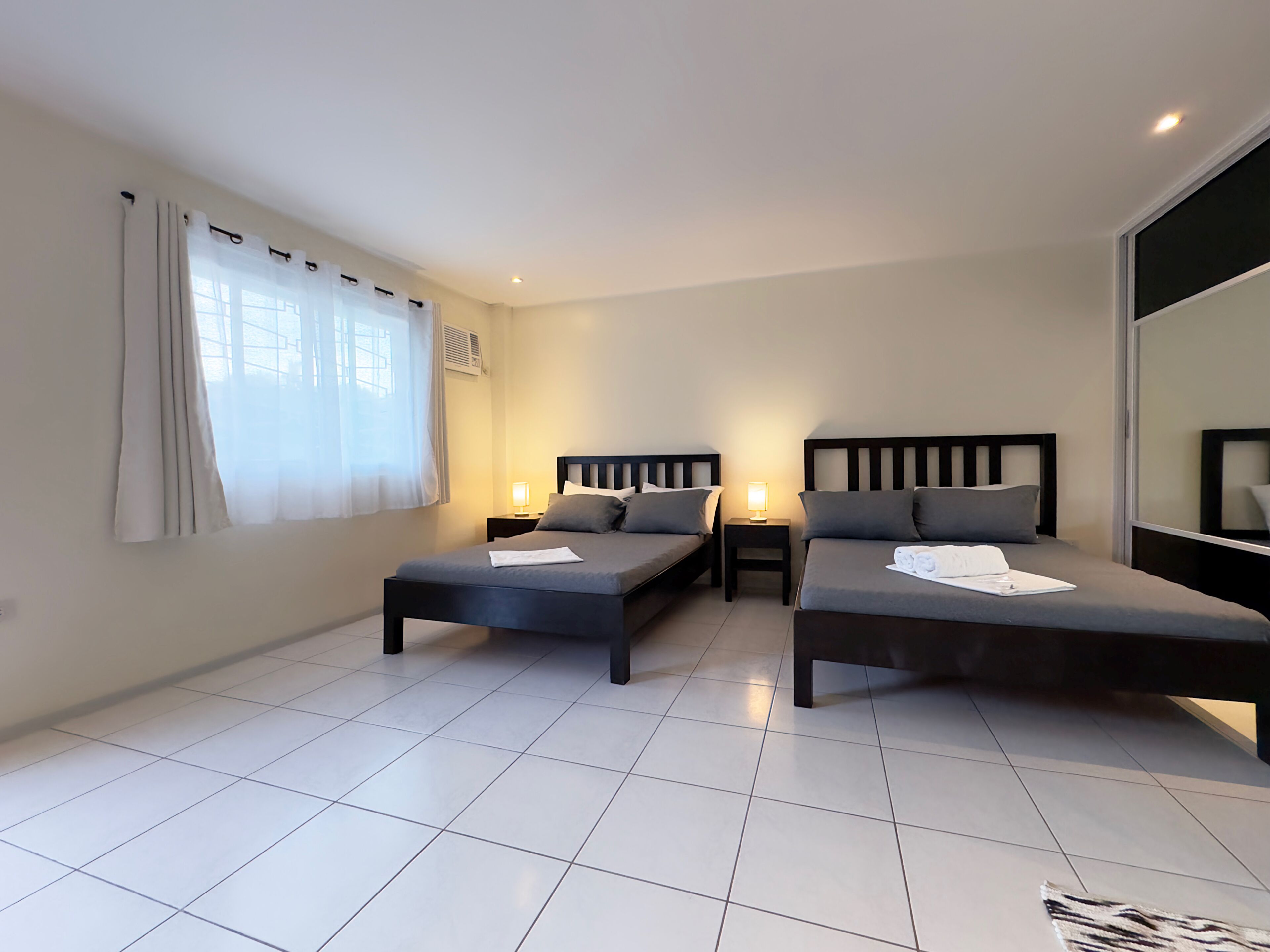 A hotel room with two single beds, a small table, and a window with curtains.