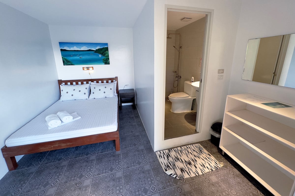 A bedroom with a bed, a bathroom with a toilet and shower, and a mirror.