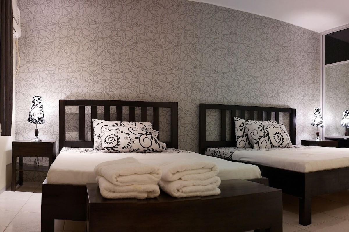 A hotel room with two beds, a large mirror, a sink, and a small stool.