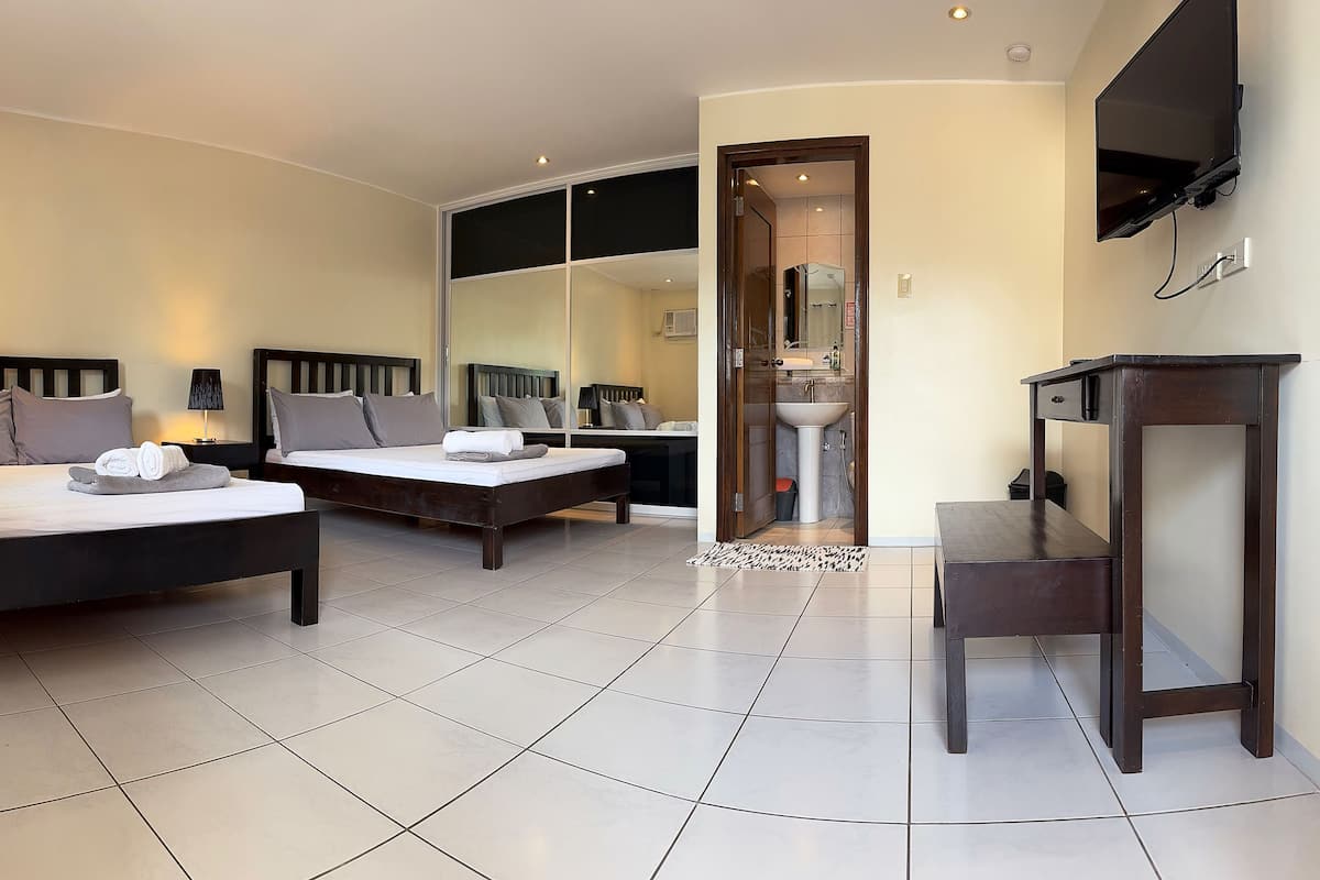A modern hotel room with two beds, a TV, a desk, and a bathroom visible through an open door.