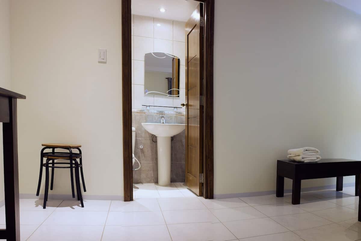 A bedroom with a bed, bedside tables, a nightstand, a chair, and a bathroom visible through an open door.