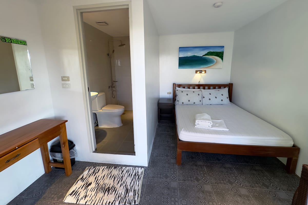 A hotel room with a wooden bed, a bathroom with a shower, a small wooden table, and a rug.