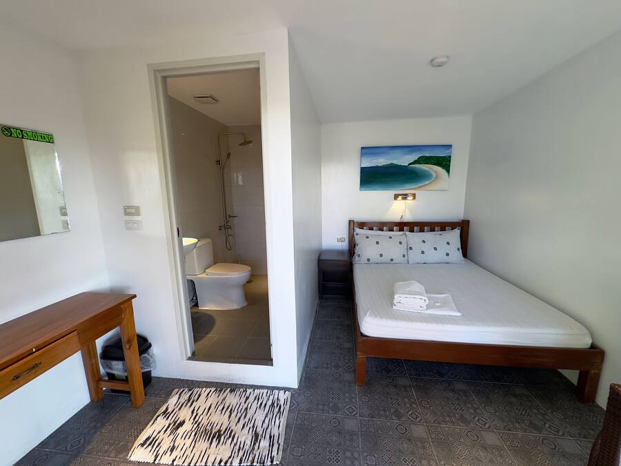 Een hotelkamer met een houten bed, een badkamer met douche, een klein houten tafeltje en een vloerkleed.