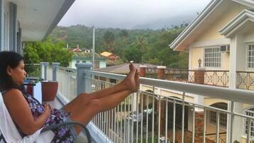 Un balcón con una persona sentada, con vistas a una zona residencial con casas y vegetación.