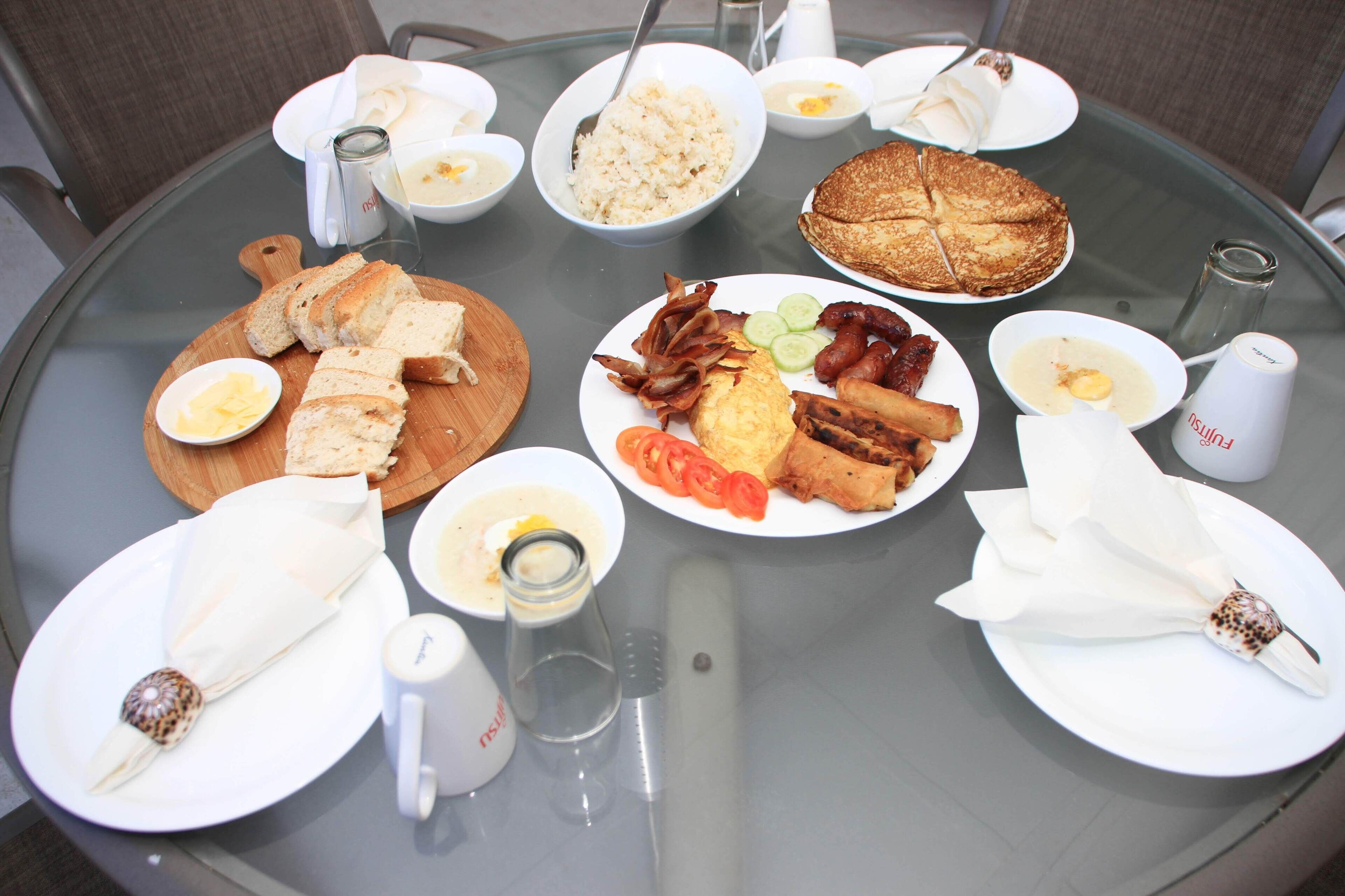 Une table ronde en verre, sur laquelle sont disposés divers aliments pour le petit-déjeuner, notamment du pain, des œufs, du bacon et des légumes.