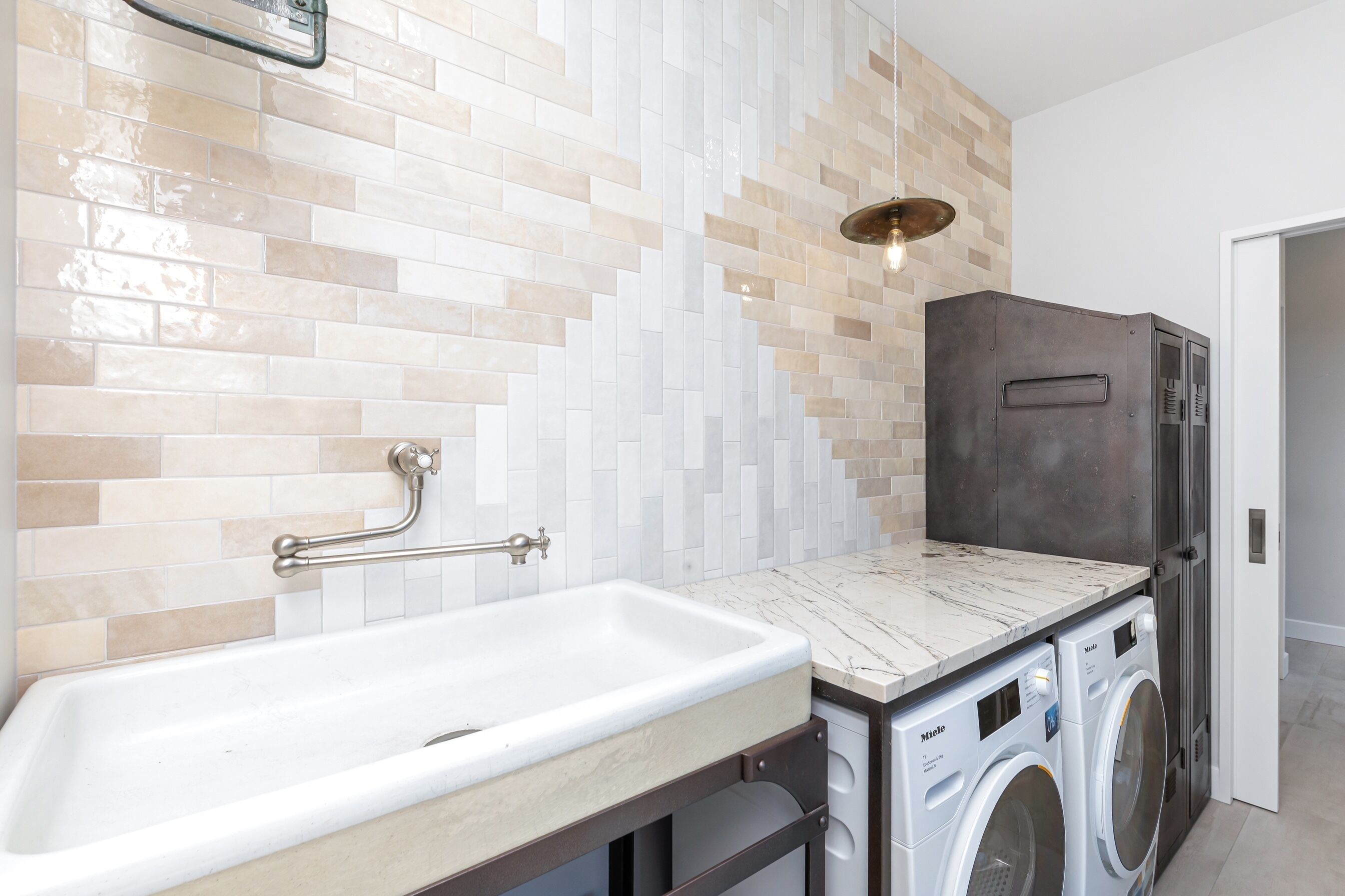 A modern bathroom with a marble countertop, a built-in washing machine, and a tiled wall.