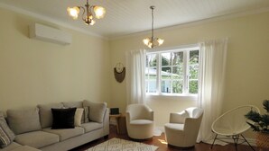 Ein Wohnzimmer mit einer Couch, zwei Sesseln, einem Couchtisch und einem großen Fenster mit Vorhängen.