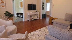 Ein Wohnzimmer mit einem weißen Konsolentisch, einem grauen Sofa, einem weißen Sessel und einem gemusterten Teppich.
