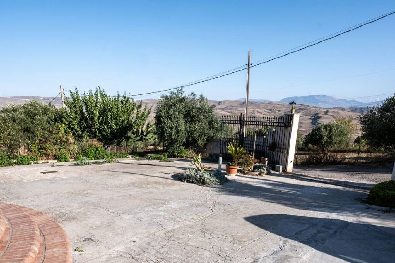 Un carril apèrvid que condueix a una entrada amb porta i vista als turons al fons.