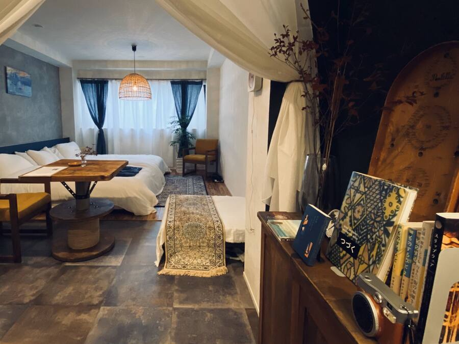 Een kamer met een bed, een houten tafel, een kleine bank, een boekenkast en een grote spiegel.