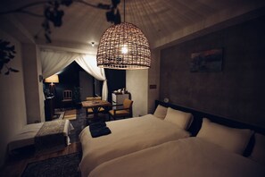 A hotel room with two beds, a dining area, and a large hanging light fixture.