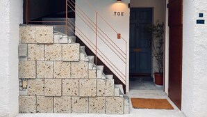 A staircase with a metal railing, a wall-mounted light labeled "TOE," and a door with a blue frame. - TOE LIBRARY (Tokyo)