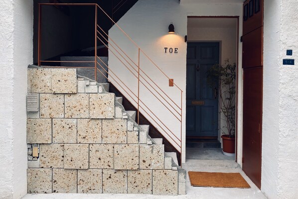 A staircase with a metal railing, a wall-mounted light labeled "TOE," and a door with a blue frame.