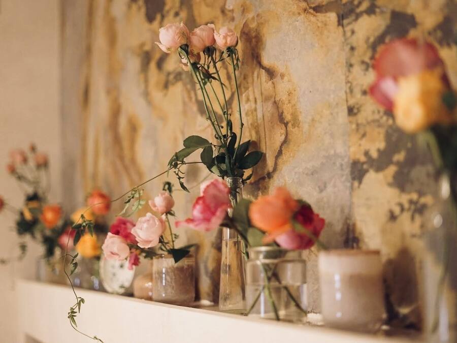 A shelf with various glass vases containing flowers, set against a textured wall.
