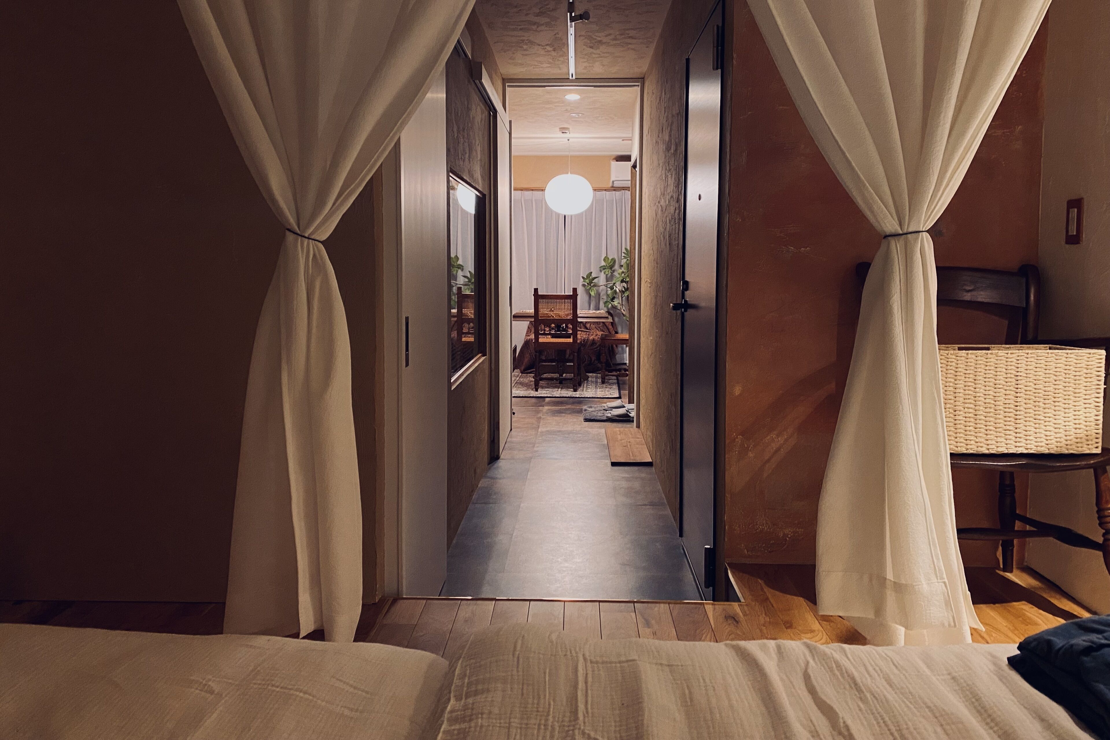 Un pasillo estrecho con una cama a la izquierda y una silla a la derecha, que conduce a un comedor con una mesa y sillas.