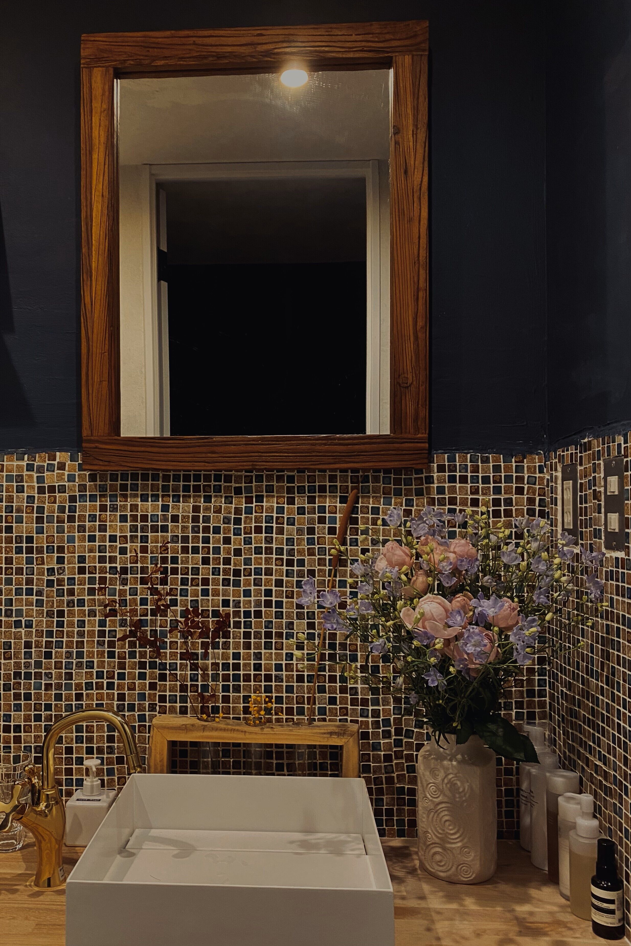 Ein Badezimmer mit einem weißen Waschbecken, einem spiegelnden Wandbild mit Holzrahmen und einer gefliesten Rückwand.
