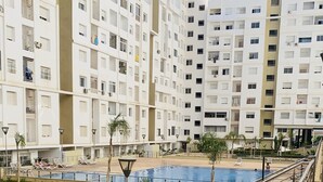 Un edificio moderno con varios pisos, piscina y un área ajardinada con senderos y barandillas.