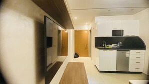 Un pasillo estrecho que conduce a una cocina con armarios blancos, una encimera negra y un microondas.