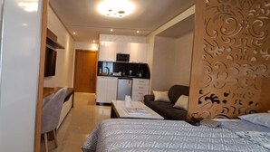 Una habitación de hotel moderna con una cama, un sofá, una pequeña mesa de comedor y una kitchenette al fondo.