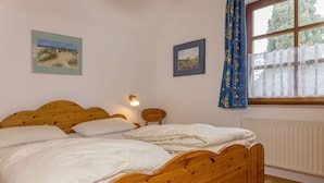 A bedroom with a wooden bed, white bedding, a nightstand with a lamp, and two framed pictures on the wall. - Völlig Ausgeglichen: Die Erdgeschoss-wohnung Liegt in Unmittelbarer Nähe des Kur (Carolinensiel)