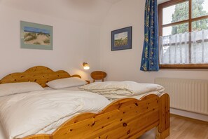 Ein Schlafzimmer mit einem hölzernen Bett, weißer Bettwäsche, einem Nachttisch mit Lampe und zwei gerahmten Bildern an der Wand.