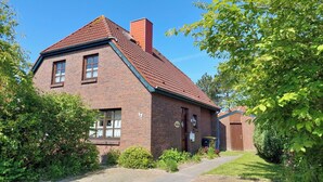 A two-story brick house with a sloped roof, a chimney, and a small front yard with bushes and a pathway. - Völlig Ausgeglichen: Die Erdgeschoss-wohnung Liegt in Unmittelbarer Nähe des Kur (Carolinensiel)