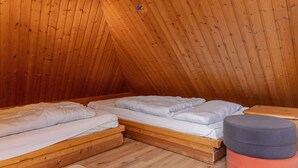 A small, cozy attic bedroom with two wooden bunk beds, a round ottoman, and a wooden bench. - Einfach mal Ausspannen: Die Obergeschoss-wohnung Liegt in Unmittelbarer Nähe ein (Carolinensiel)