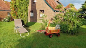 A brick house with a sloped roof, a lawn, a lounge chair, and a wheelbarrow. - Einfach mal Ausspannen: Die Obergeschoss-wohnung Liegt in Unmittelbarer Nähe ein (Carolinensiel)