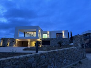 A modern two-story house with a stone facade and a well-lit entrance. - Architect-designed villa with superb view over the bay of Calvi, between sea and mountains (Calvi)