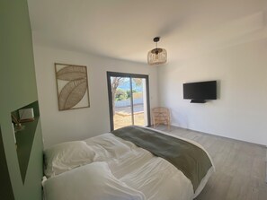 A bedroom with a bed, a television, a wicker chair, and a large window. - Architect-designed villa with superb view over the bay of Calvi, between sea and mountains (Calvi)