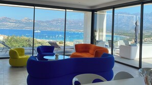 Een moderne woonkamer met grote ramen en een prachtig uitzicht op zee en bergen.