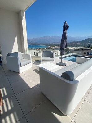 A modern outdoor seating area with white sofas and a pool, overlooking a coastal landscape with mountains in the distance. - Architect-designed villa with superb view over the bay of Calvi, between sea and mountains (Calvi)