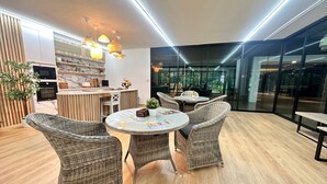 A modern interior with wicker furniture, a round glass table, and a kitchen area with built-in appliances. - Herma Hotel (Bang Phli)